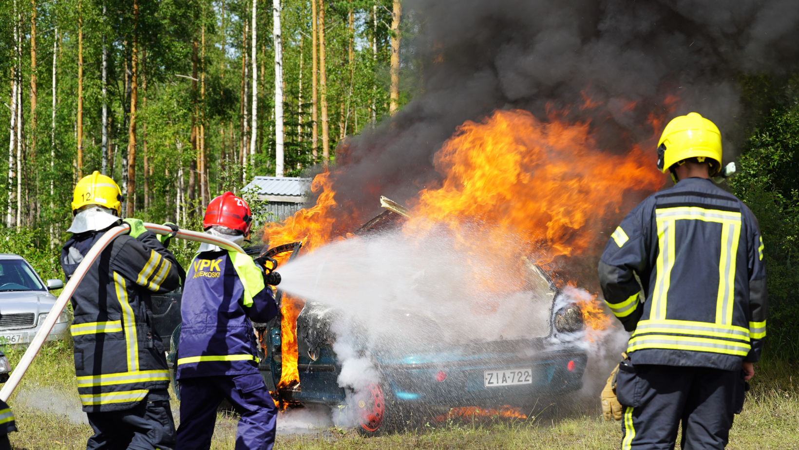Palokuntanuoret sammuttavat palavaa autoa.